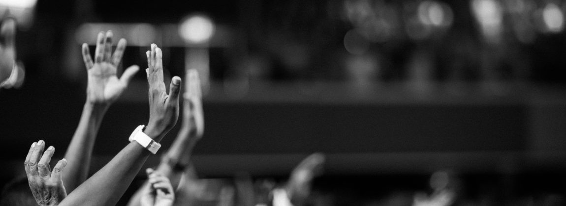 Black and white image of audience with hands raised, capturing concert energy.